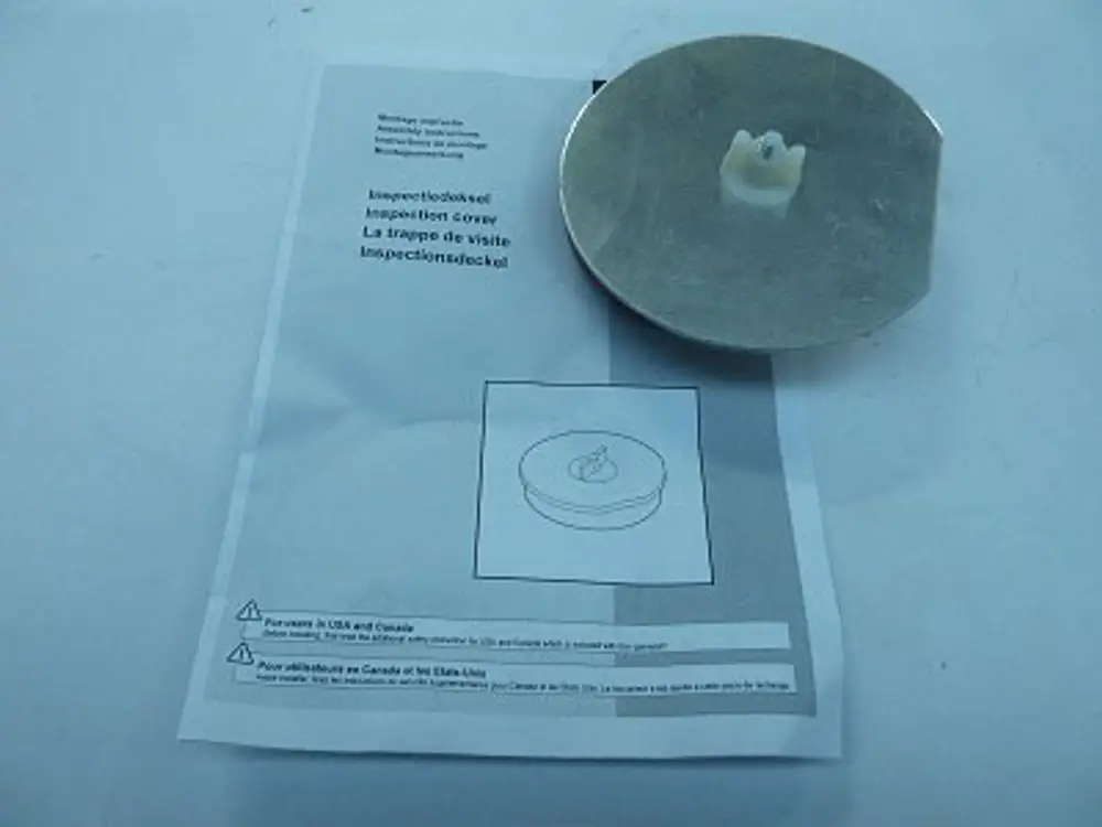 Runde Abdeckung von Remeha mit Anleitung. Die Abdeckung zeigt eine zentrale Erhebung und ist auf einem mit Information bedruckten Blatt platziert.